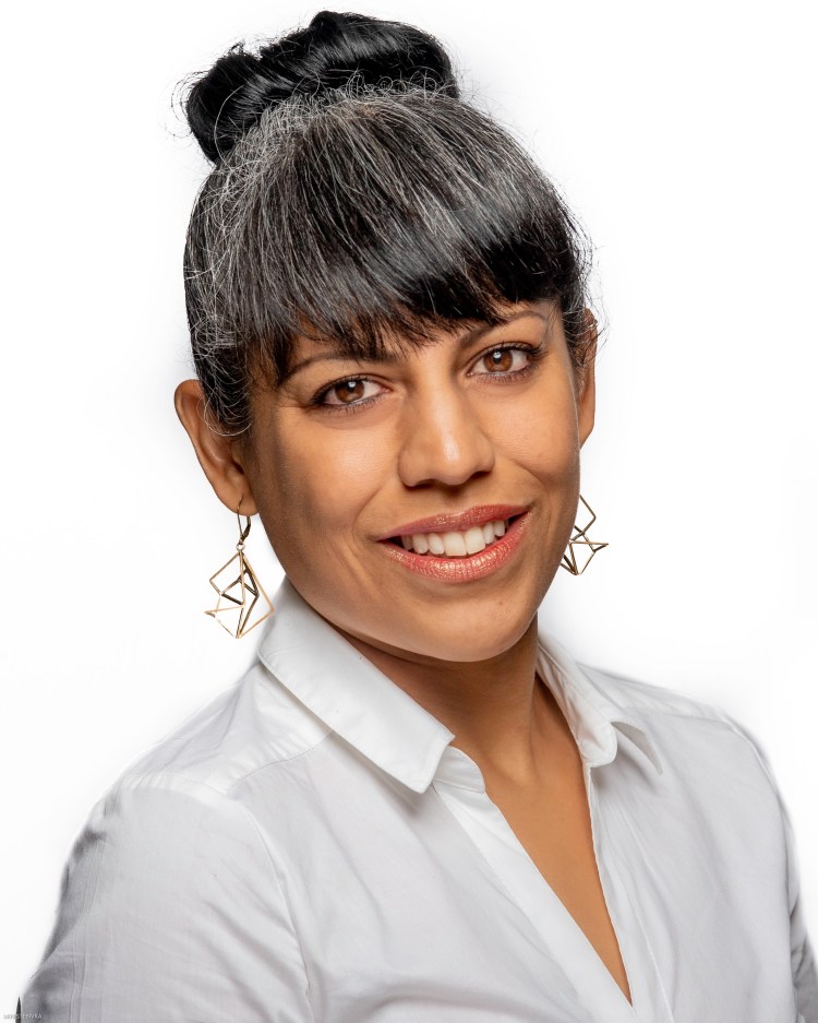 Photo is a headshot of Montserrat with her hair in a bun with bangs, dangling earrings, and a white blouse.