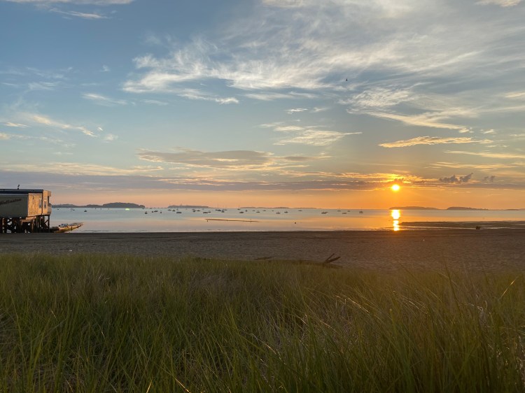 Photo is of a sunrise above the beach.