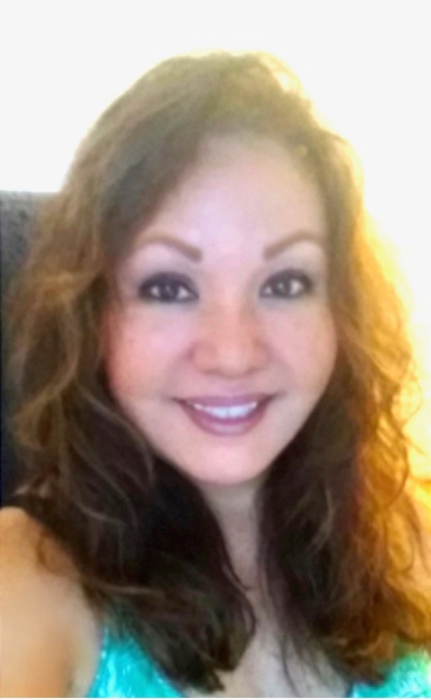 Photo is of Grace Barut. She is wearing a turquoise shirt. Her hair is down. There is the shine of a light in the background.